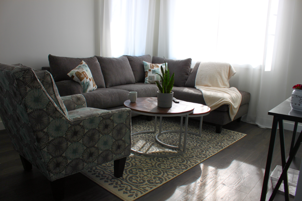 An inviting living room with a couch, table, and chair, is bathed in sunlight.