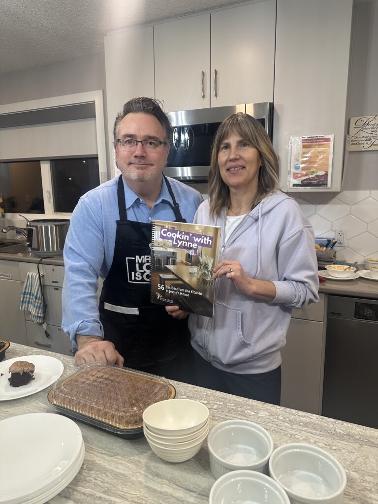 Two people in a kitchen holding the Cookin' with Lynne cookbook.