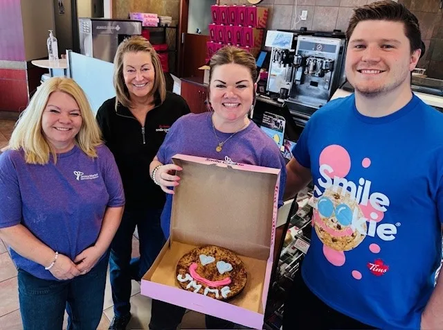 Four people at the Flower Stop holding a box with a giant Smile Cookie inside.