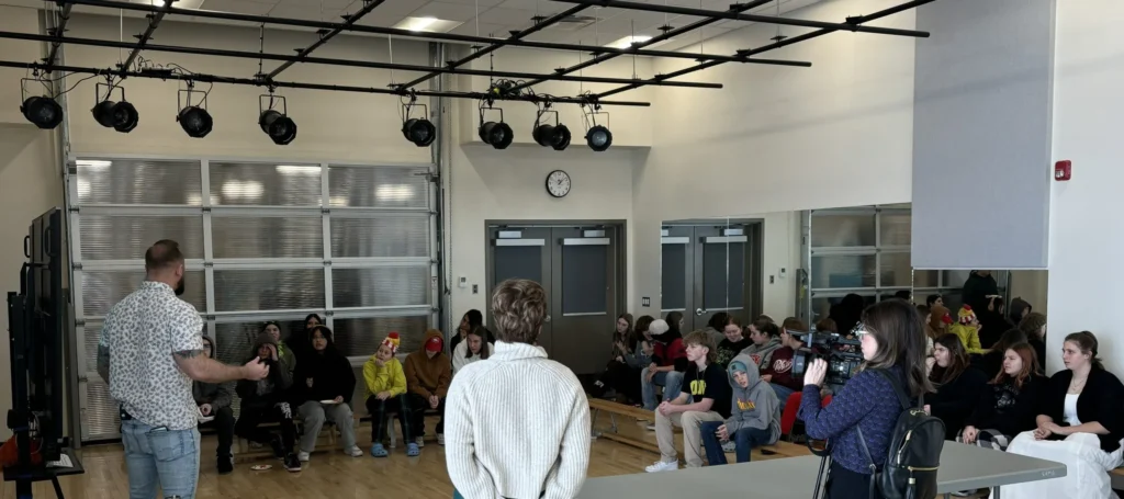 A presenter speaking to a group of students seated around a gym during an Inspire Program session.