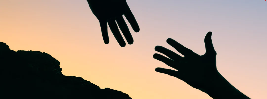 Two hands reaching toward each other against a sunset sky