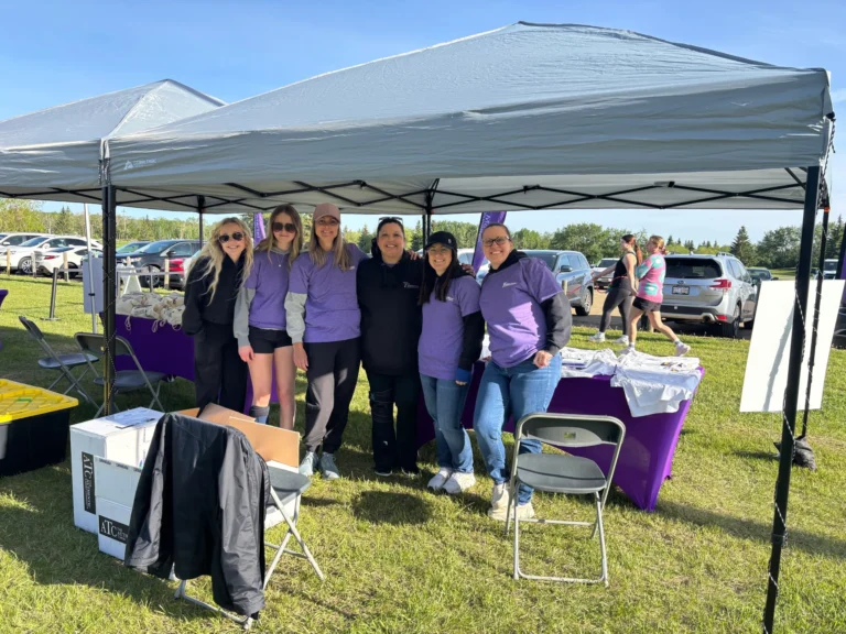 Volunteers in purple shirts under an event tent at a JMMF event